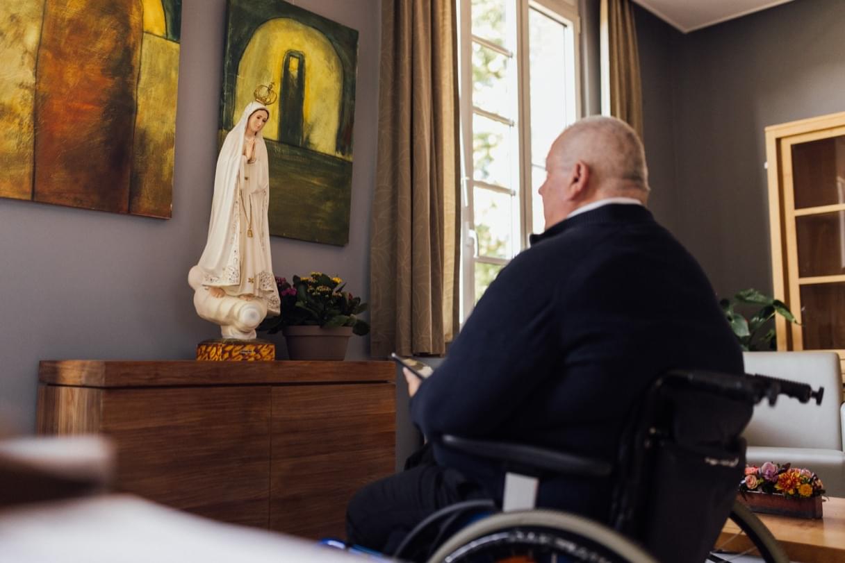 Wilfried in zijn rolstoel, kijkend naar een Mariabeeld