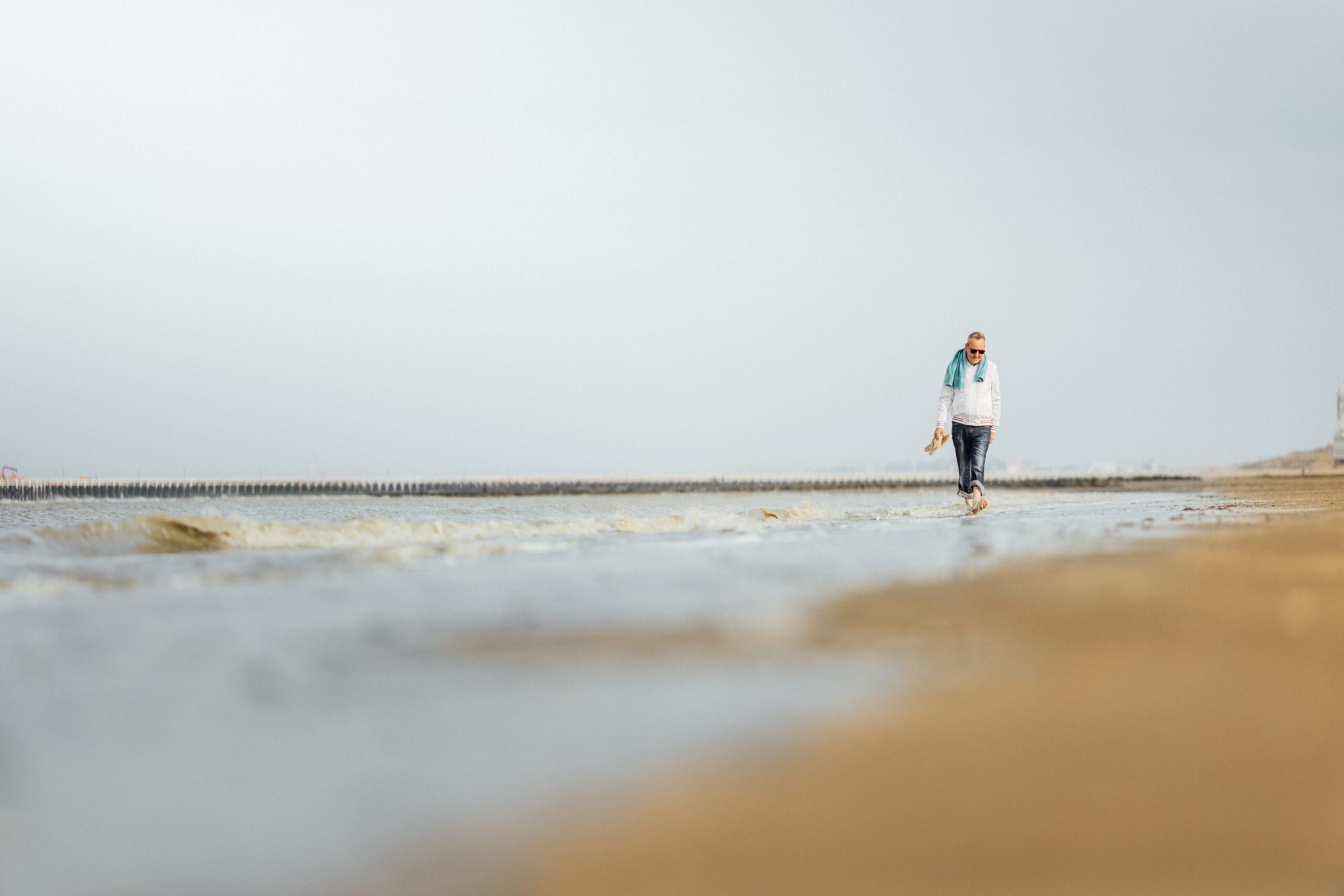 Man die met blote voeten op het strand wandelt